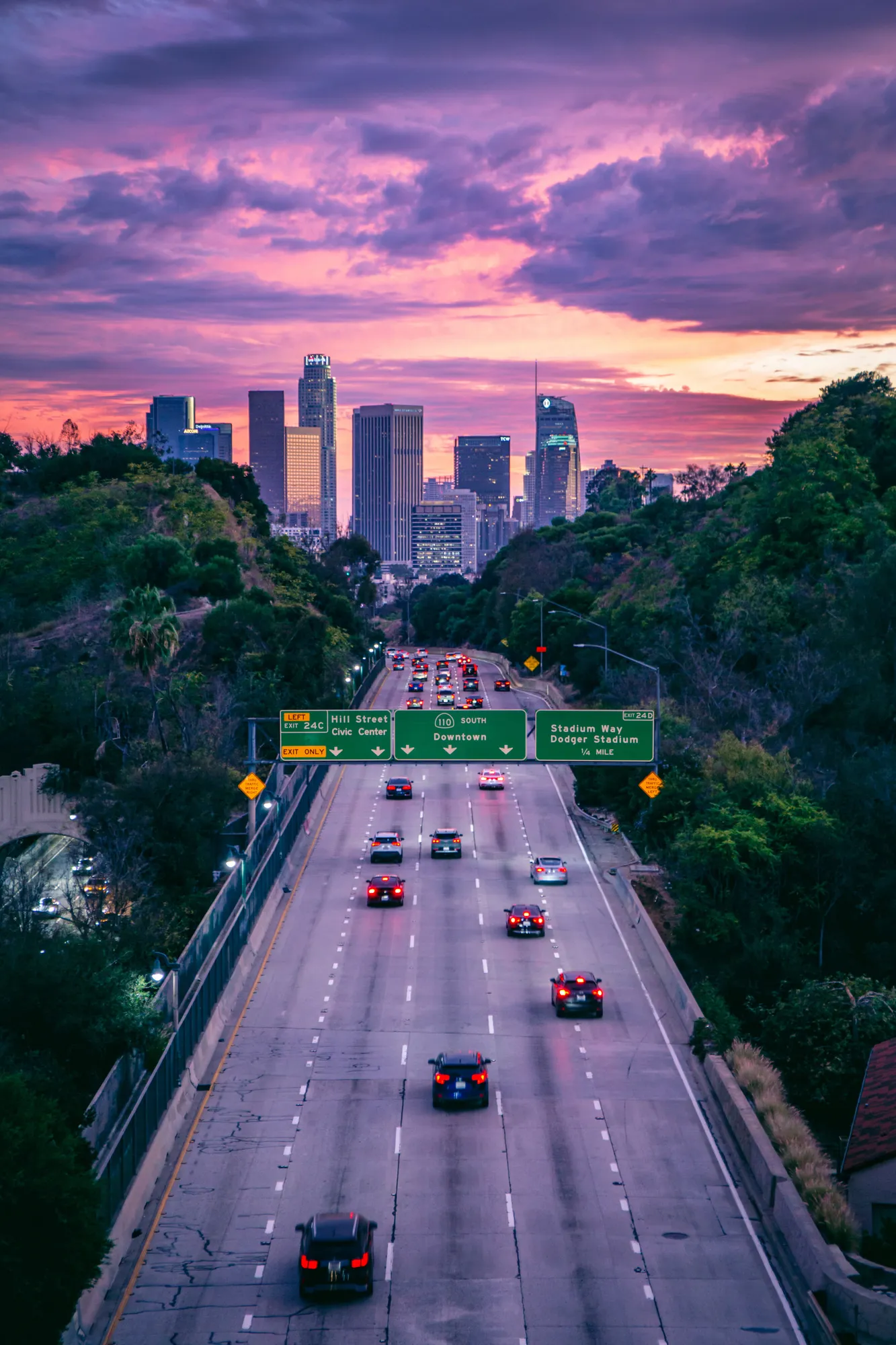 A freeway running towards the skyscrapers under a violet sunset sky. Photograph by Stefano Paolucci