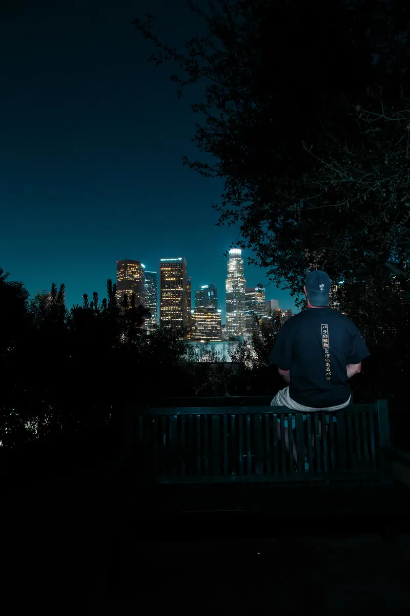 A man on a bench looking at the lit-up skyline at night. Photograph by Stefano Paolucci